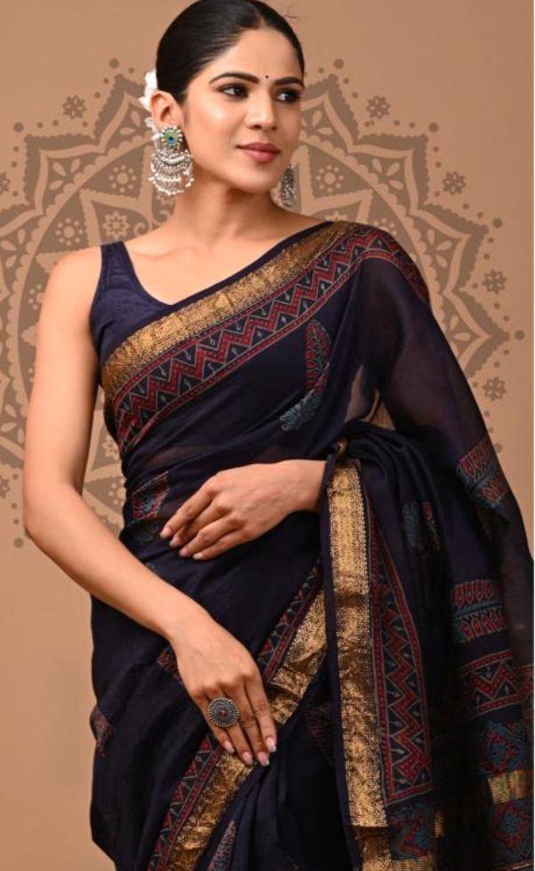 Woman wearing a dark blue saree with gold and red patterns against a decorative brown background