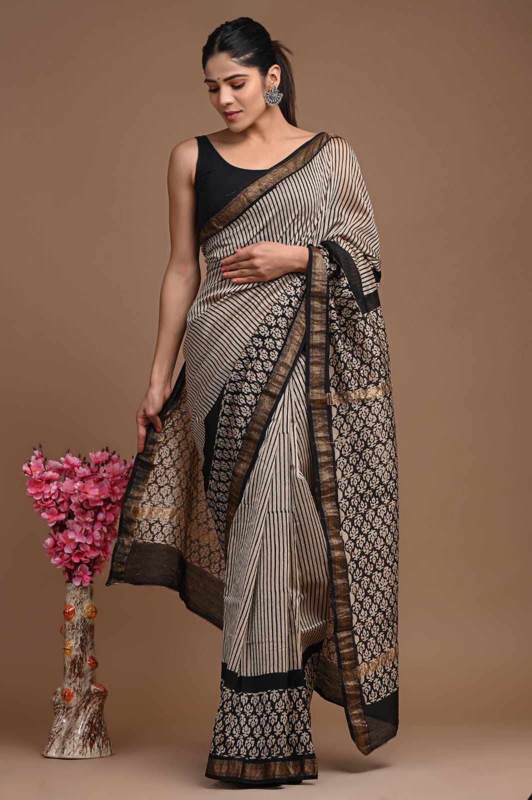 Woman wearing a patterned saree holding flowers against a brown background