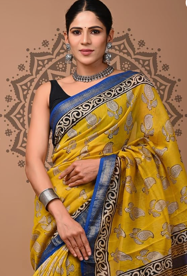 Woman wearing a yellow saree with a blue border against a decorative brown background