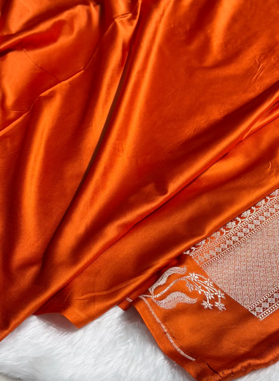 Close-up of orange fabric with intricate white embroidery on a white background