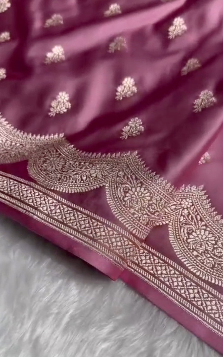 Close-up of a pink fabric with intricate silver embroidery on a fluffy gray surface.