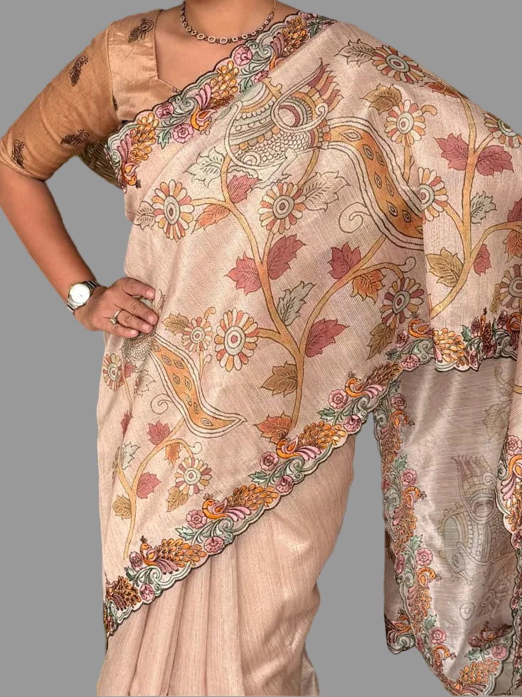 Woman wearing a beige saree with floral patterns, standing outdoors with greenery in the background.