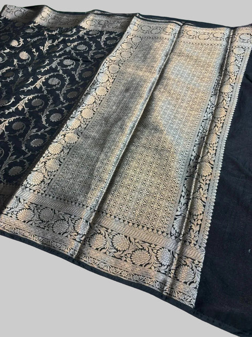 Black saree with intricate gold patterns on a green grass background