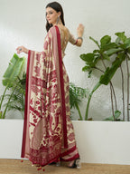 Woman in a traditional saree with red and white patterns, standing against a white wall with green plants.