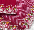Red fabric with intricate white, green, and pink embroidery held by a hand.