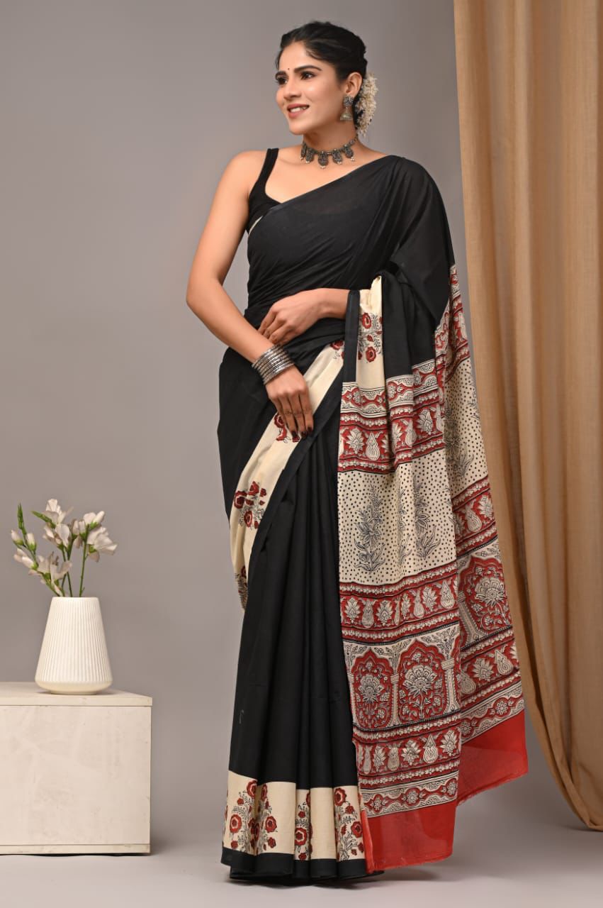 Woman wearing a black and patterned saree with a vase and curtain in the background