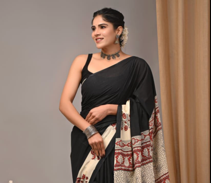 Woman wearing a black saree with a patterned border against a neutral background