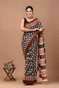 Woman wearing a black and white patterned saree with a brown border on a beige background