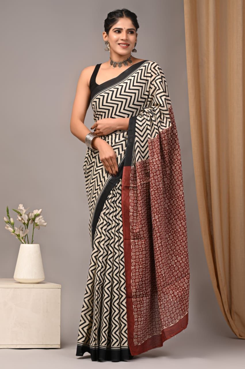 Woman wearing a black and white patterned saree with a maroon border, standing against a neutral background.