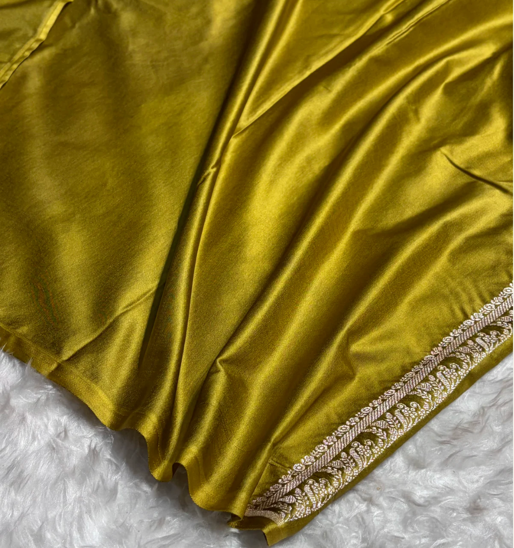 Gold fabric with intricate white embroidery on a textured white surface