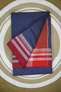 Two folded fabrics, one blue with a grid pattern and the other red with white patterns, on a circular woven mat.