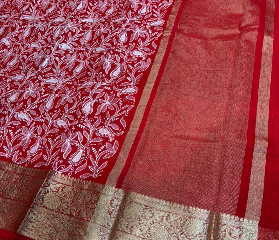 Red saree with white floral patterns and gold border on a green surface