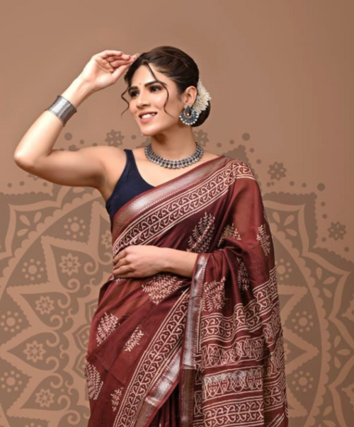 Woman wearing a maroon saree with white patterns against a brown background