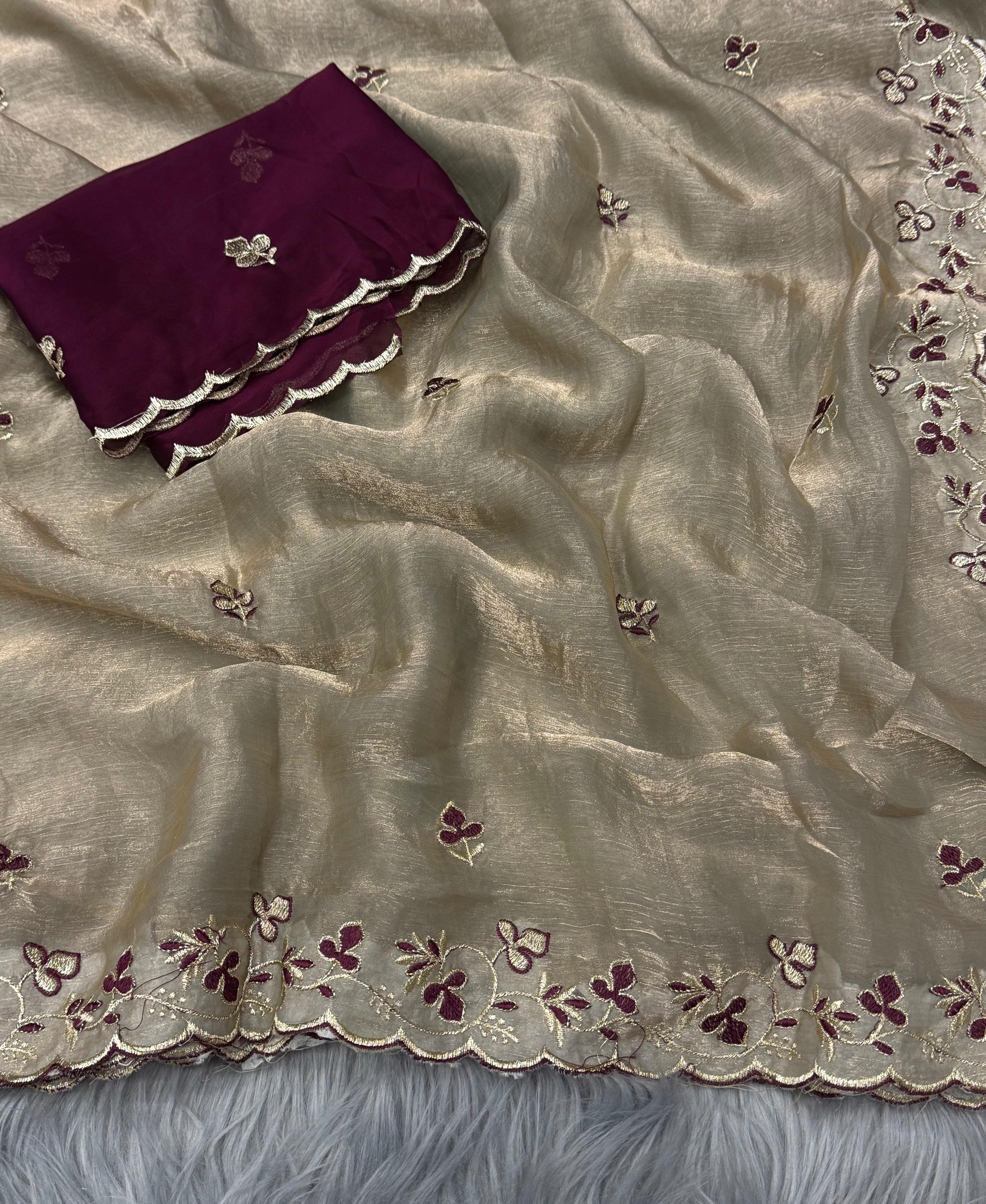 Beige saree with floral embroidery and purple blouse on a textured surface