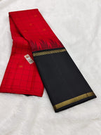 A folded red and black saree with gold zari borders and motifs, laid flat on a white textured fabric background.
