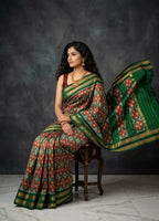 Woman in a green and red saree sitting on a chair against a dark background