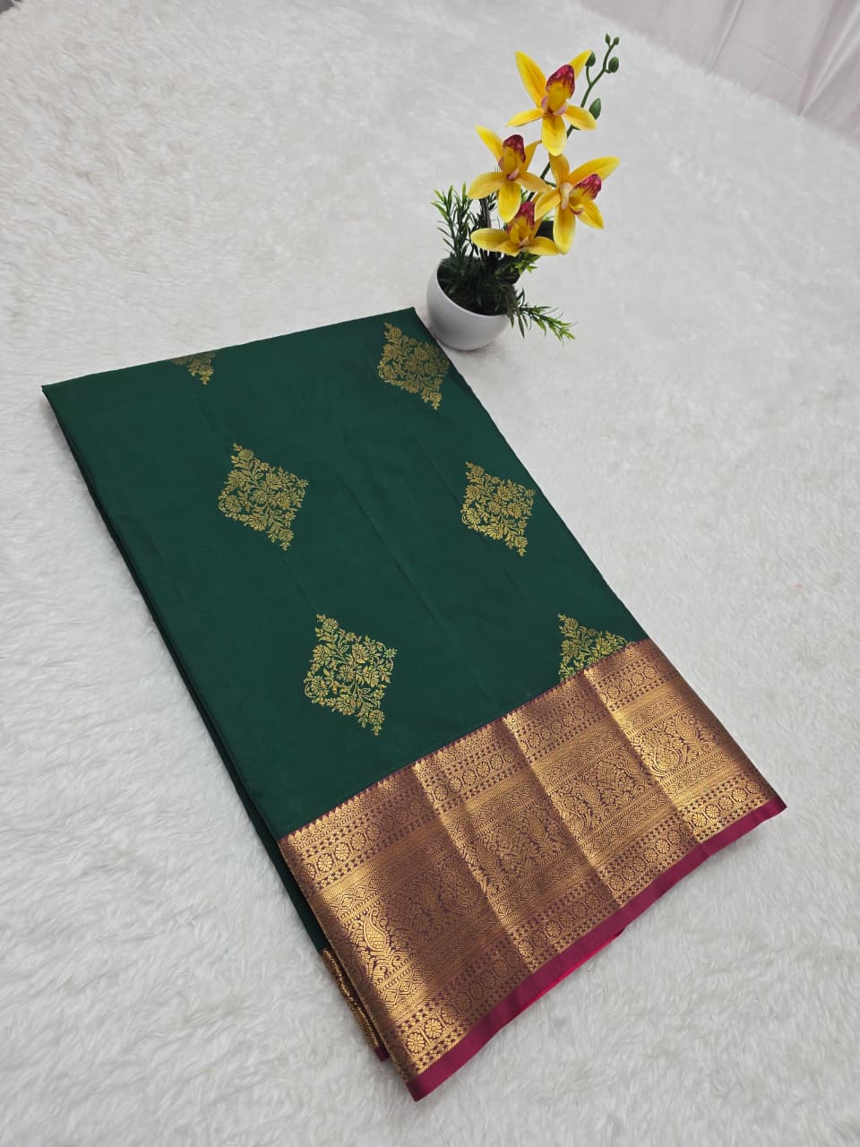 Green saree with gold border on a white surface with yellow flowers.