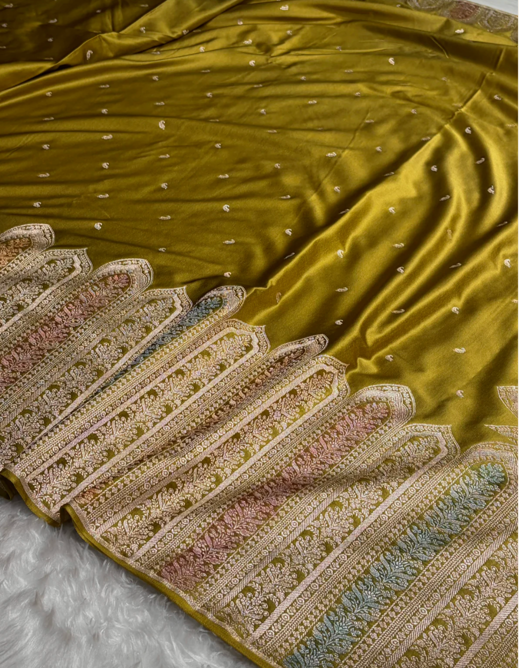 Green saree with intricate gold and multicolor embroidery on a textured surface