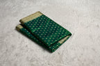 Green saree with gold patterns on a white surface, with a Zara box in the background.