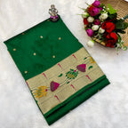 Green saree with floral patterns on a white surface, accompanied by flowers and a small statue.