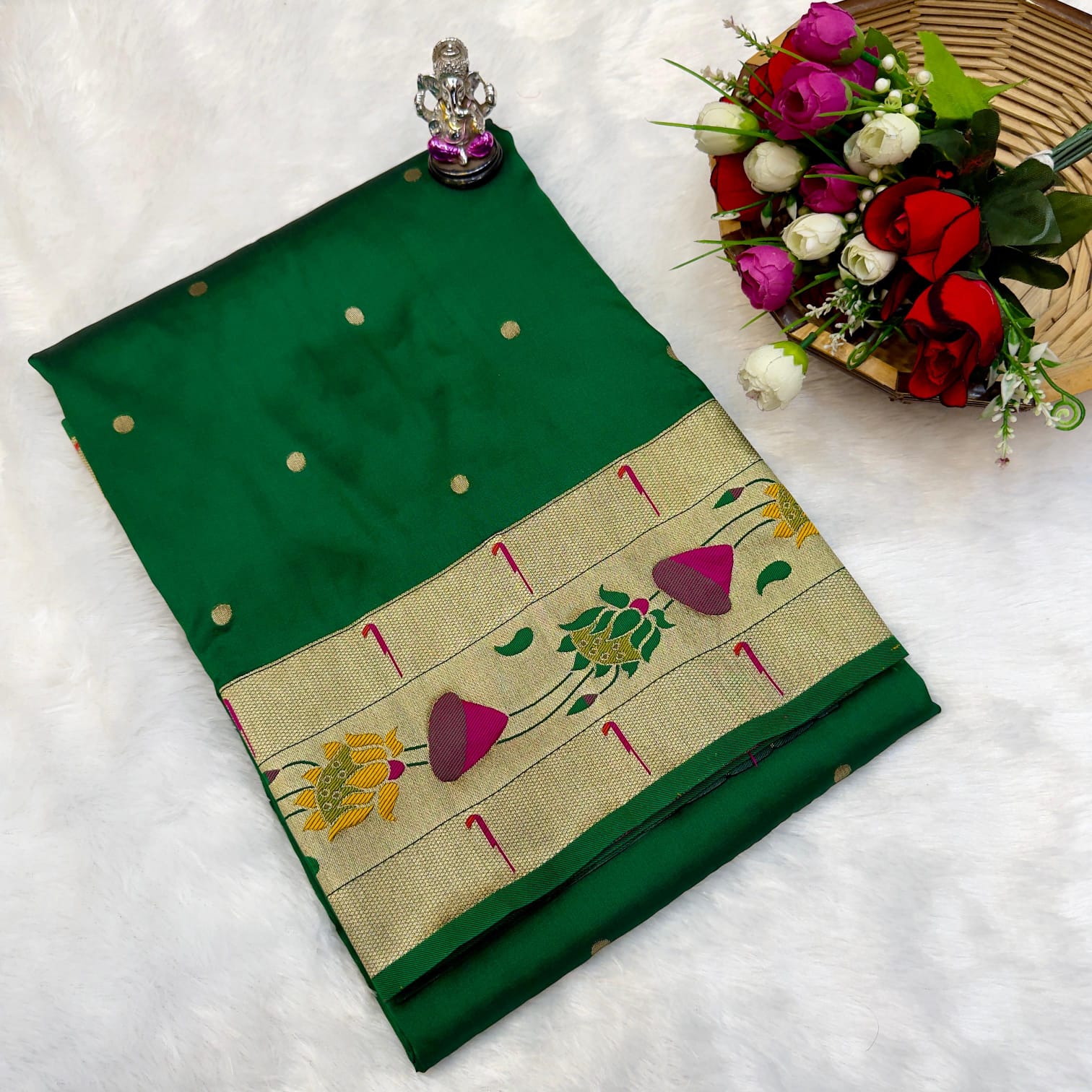 Green saree with floral patterns on a white surface, accompanied by flowers and a small statue.