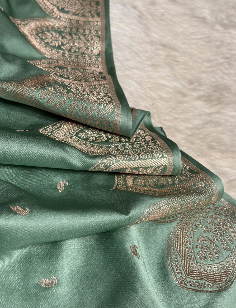 Green fabric with intricate gold embroidery on a neutral background