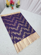 Purple saree with gold border on a white surface, with decorative flowers in the background.