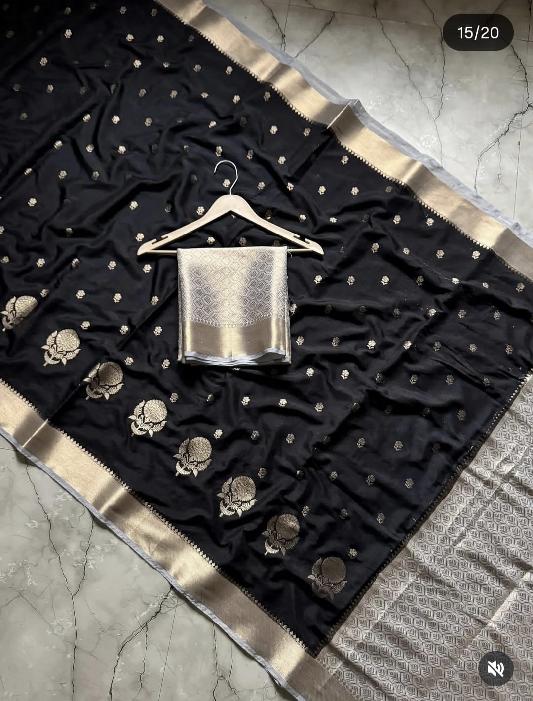Black saree with gold border and silver blouse on a hanger against a marble background