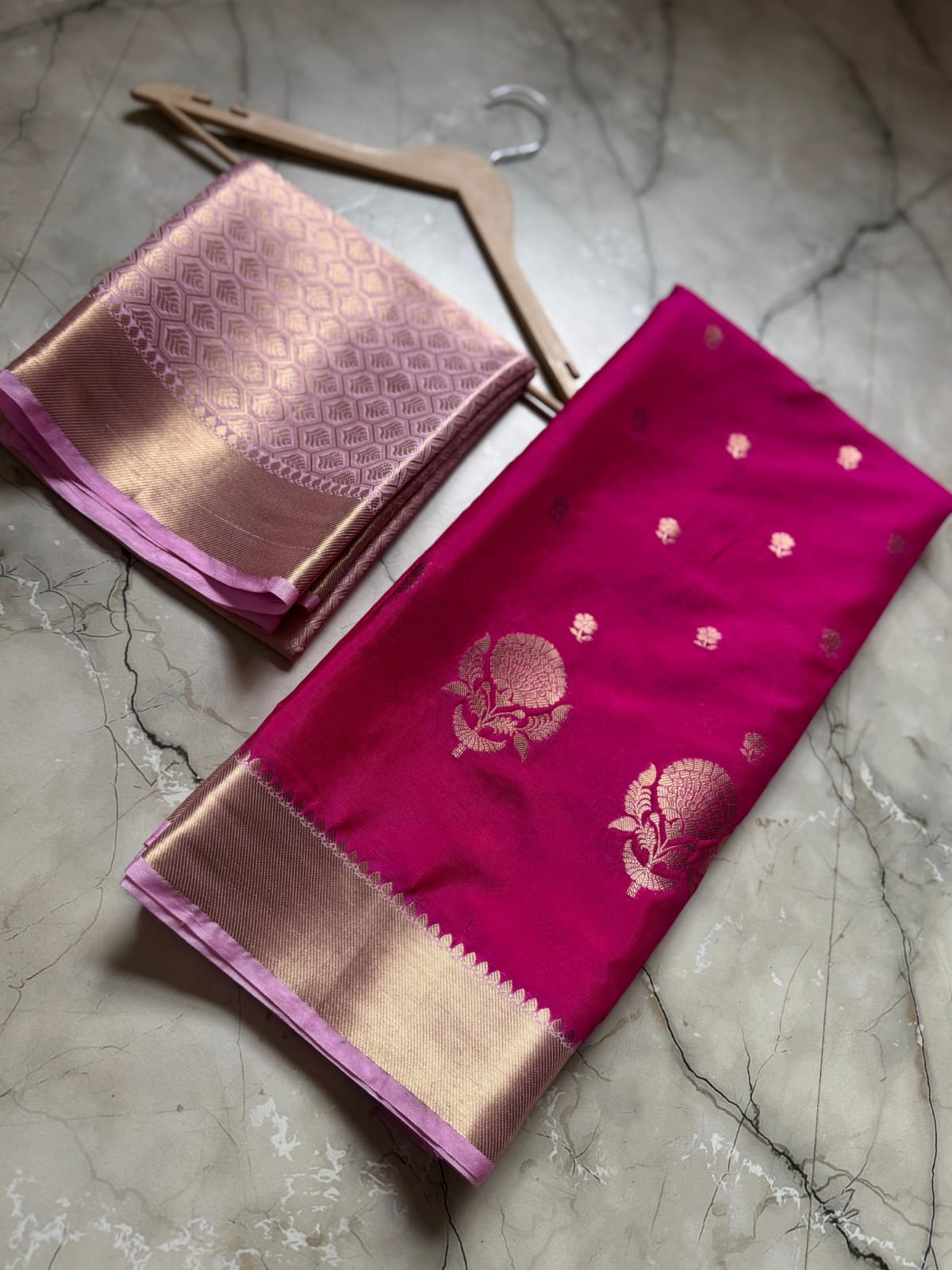 Two pink sarees with gold borders on a marble surface