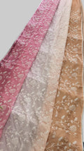 Three scarves in pink, beige, and brown with floral patterns draped over a surface with potted plants.
