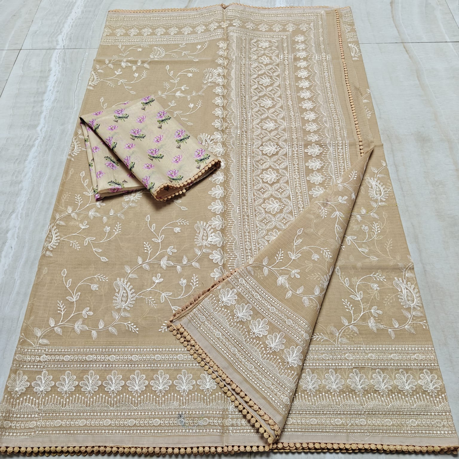 Beige fabric with white floral embroidery on a tiled floor