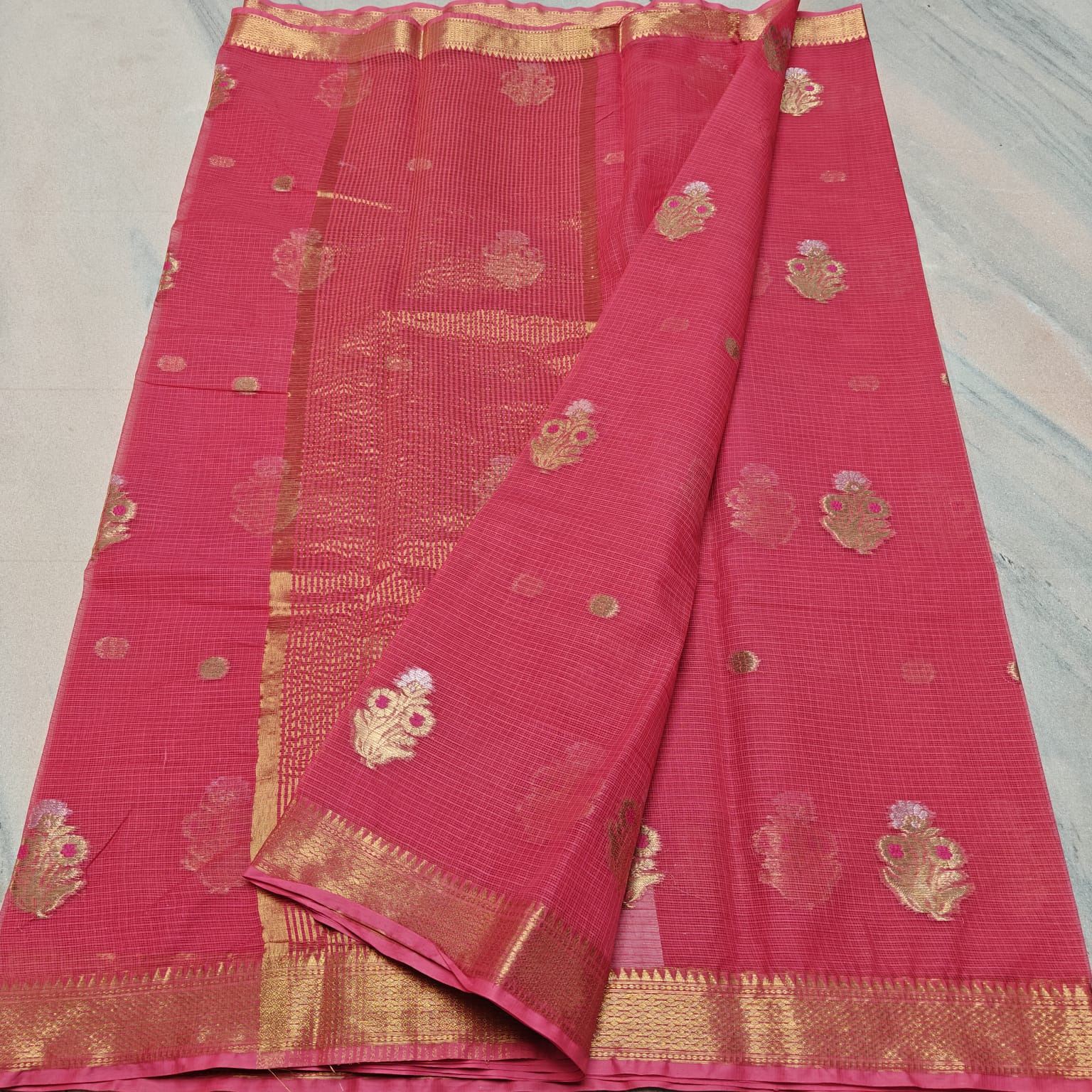 Pink saree with gold patterns on a light gray surface