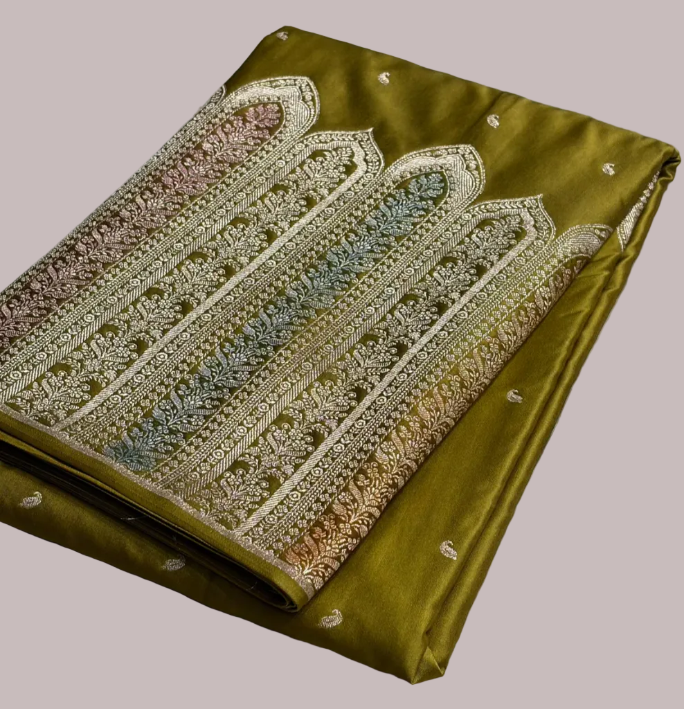 Green fabric with intricate gold embroidery on a textured surface, branded 'Zaira'.