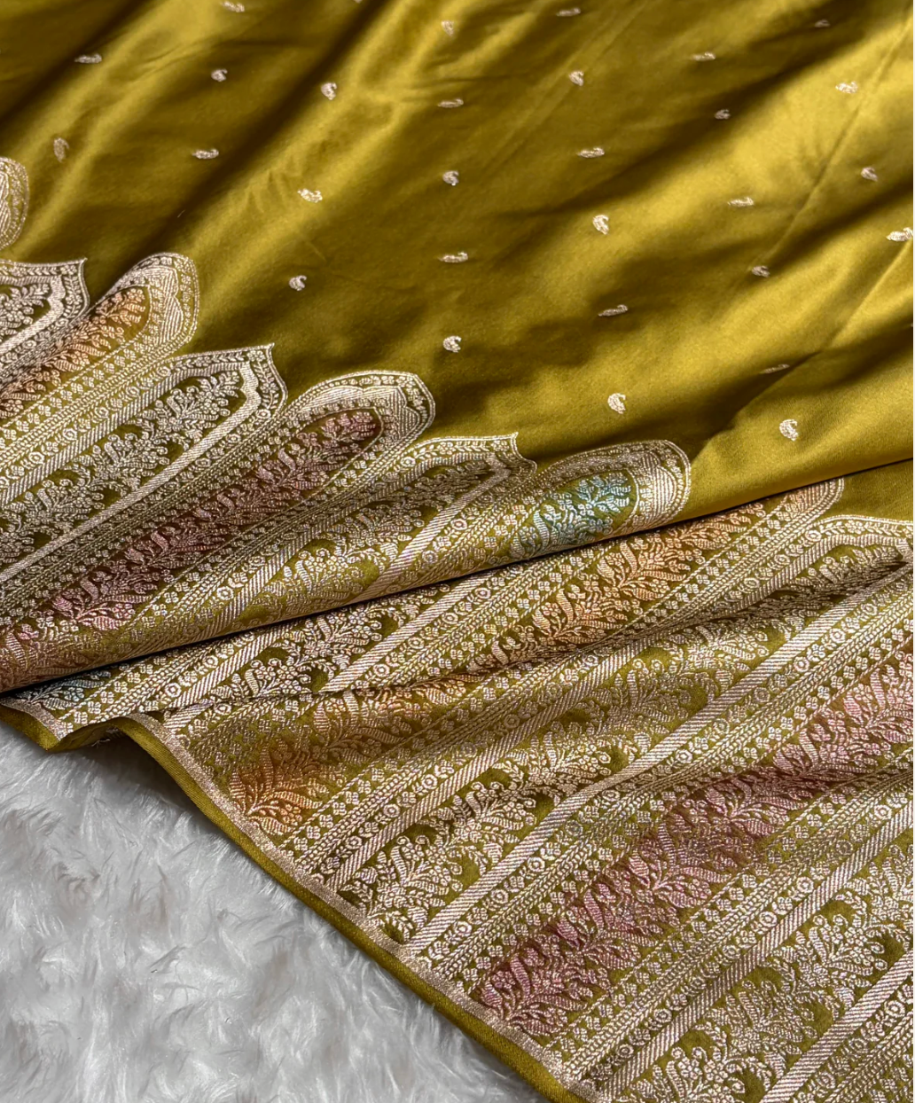 Green fabric with intricate gold and pink embroidery on a white surface