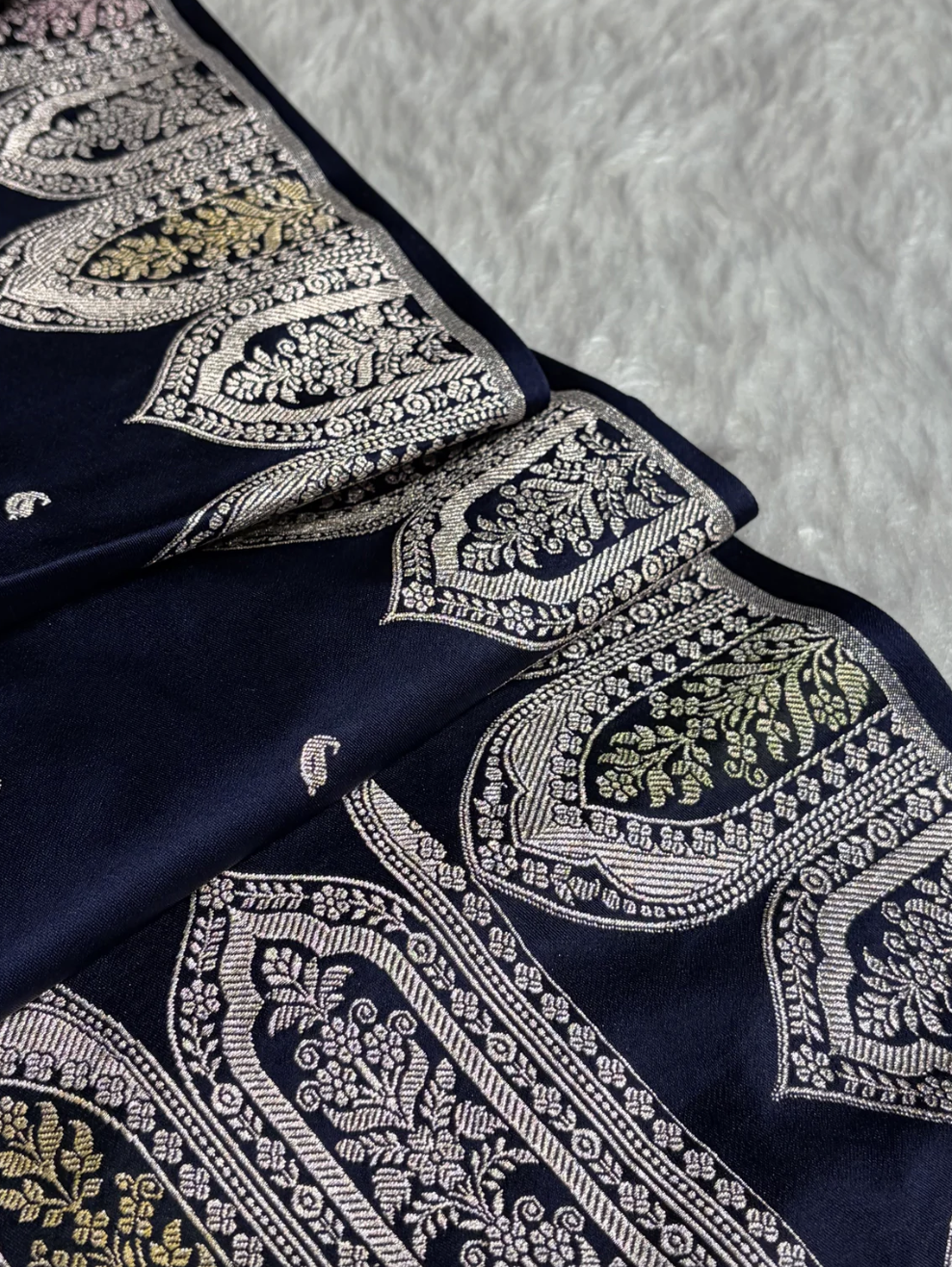Navy blue fabric with intricate white and gold embroidery on a textured gray background
