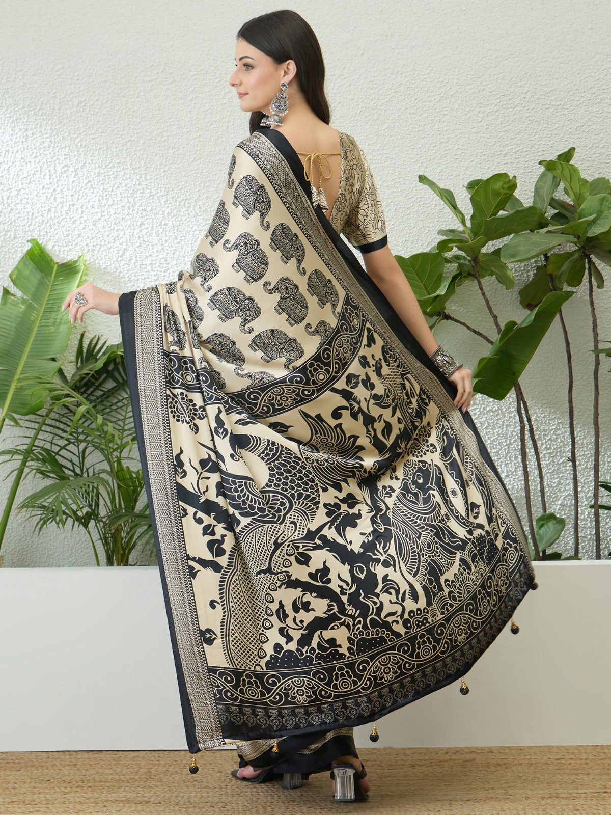 Woman wearing a black and white patterned saree with plants in the background
