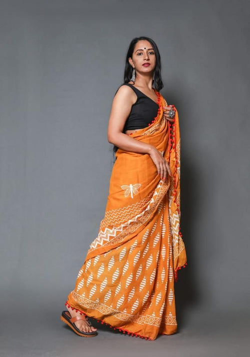 Woman wearing an orange saree with a black blouse against a gray background
