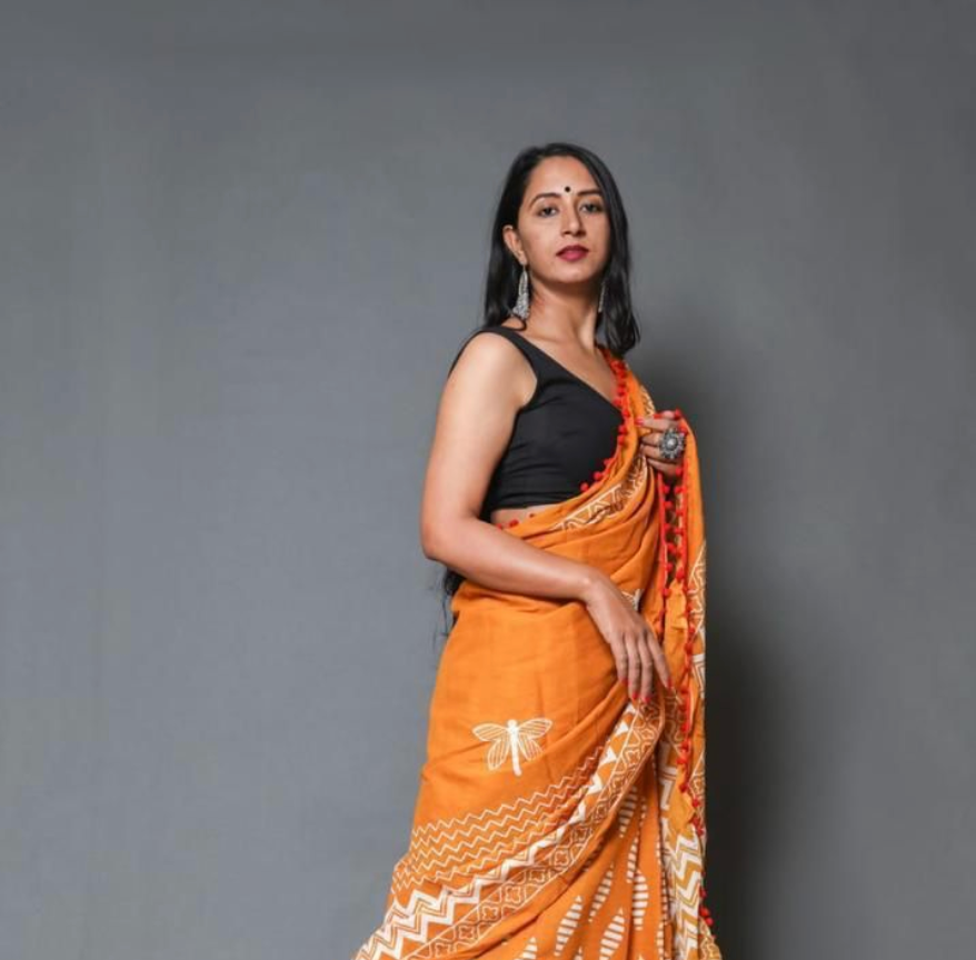 Woman wearing an orange saree with a black blouse against a gray background
