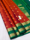 A folded red and green silk saree with intricate gold zari floral motifs and borders, displayed on a light gray surface.