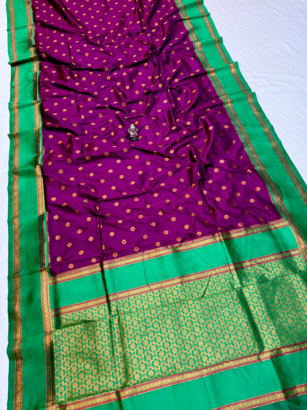 Purple saree with gold polka dots and green border on a white background