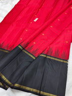 A folded red and black saree with gold zari detailing, laid out on a white fabric background.