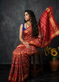 Woman in a traditional red and gold saree sitting on a chair with a dark background