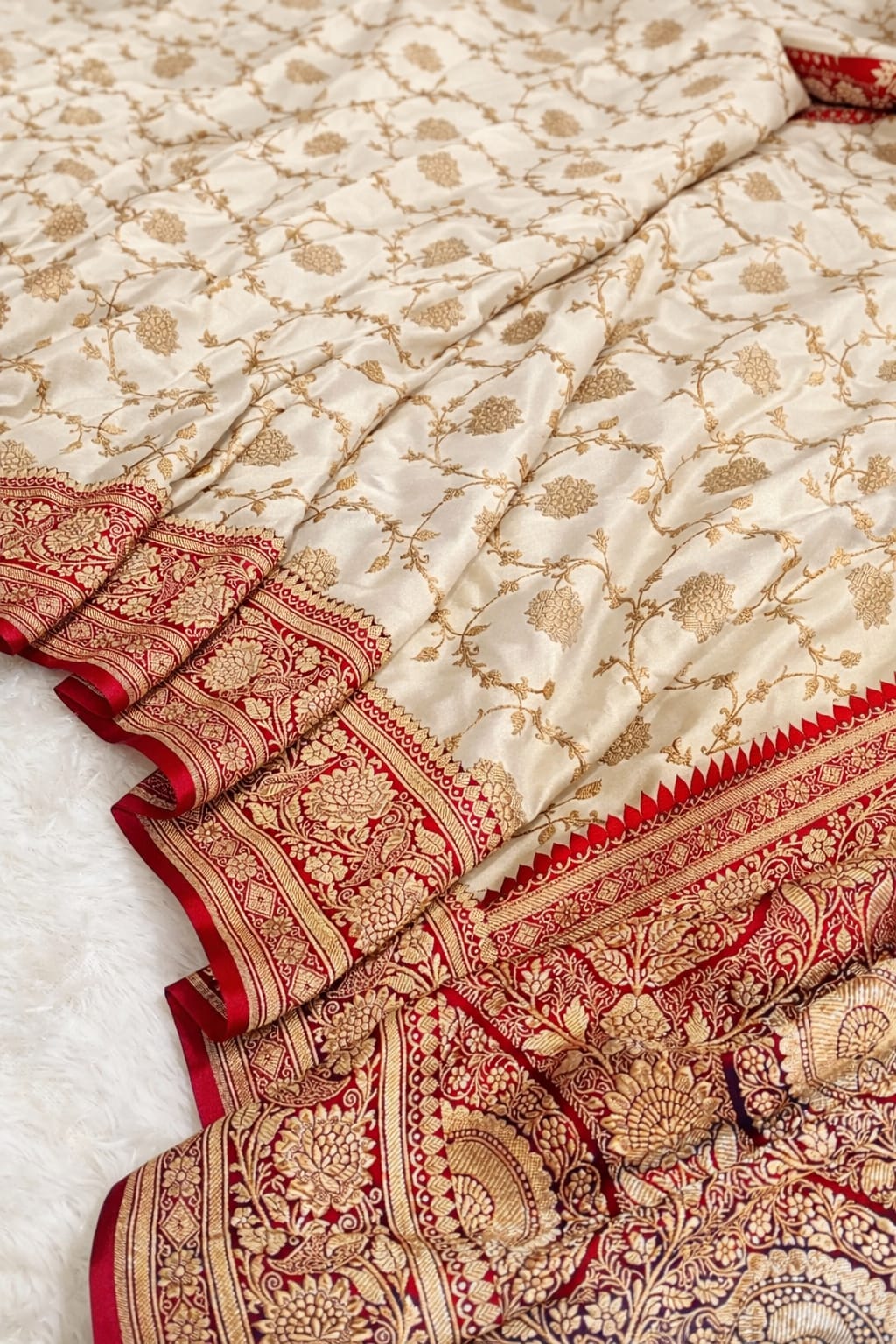 Close-up of a traditional saree with red and gold patterns on a white background