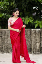 Woman in a red saree with a white blouse against a green foliage background