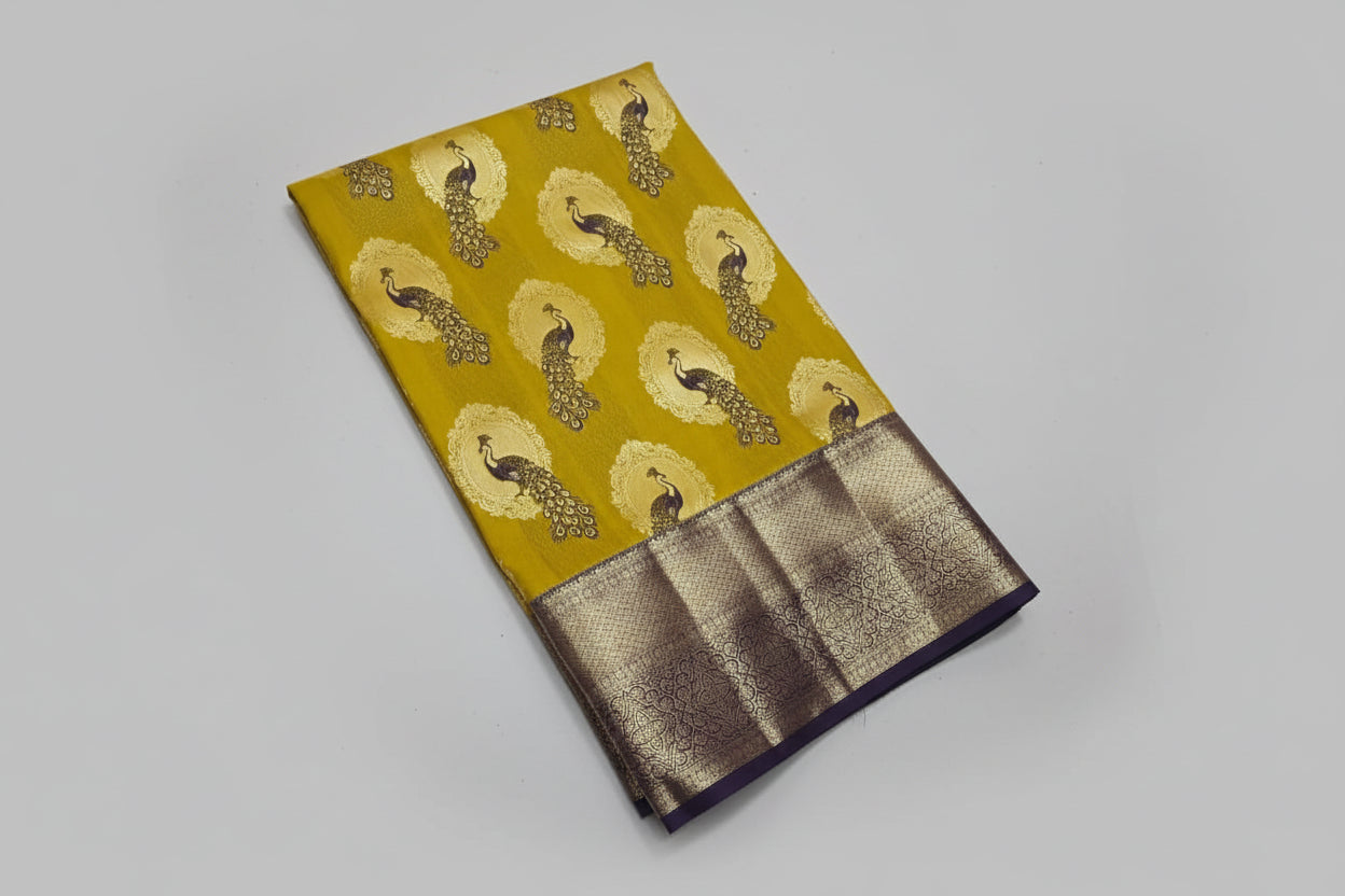 Yellow fabric with peacock pattern and brown border on a white surface with a small plant.