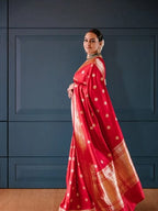 Woman wearing a red saree with gold patterns against a blue wall.