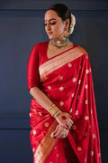Woman wearing a red saree with gold patterns against a dark background