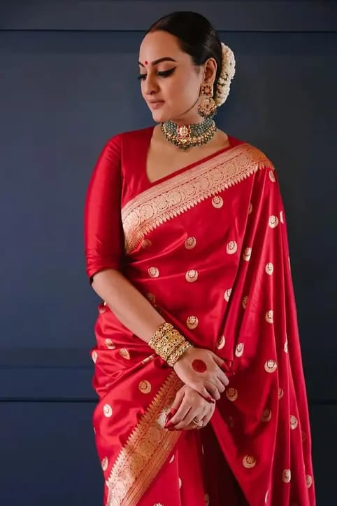 Woman wearing a red saree with gold patterns against a dark background