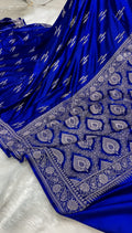 A royal blue fabric garment, likely a saree or dress, featuring intricate silver zari embroidery and a heavily embellished border with paisley and floral motifs.