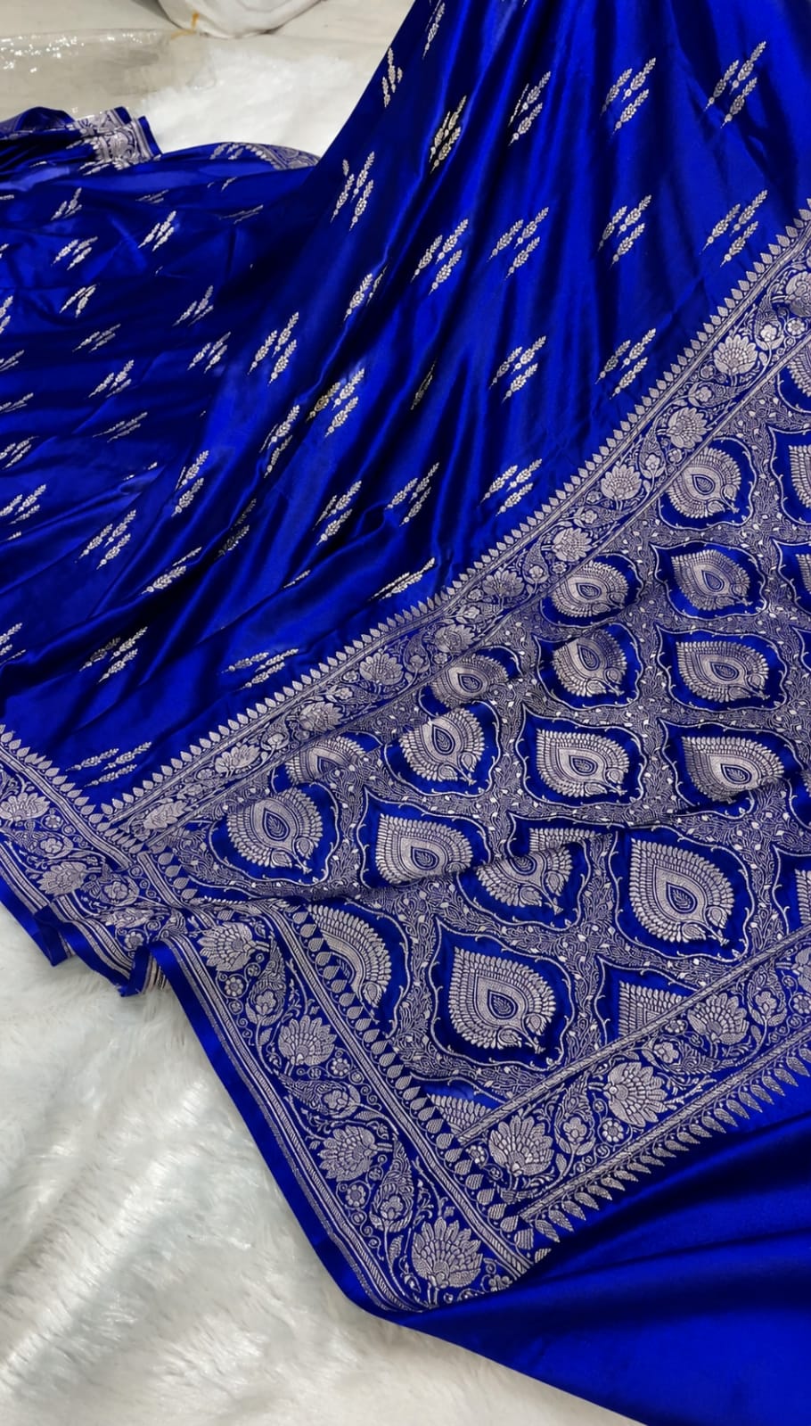 A royal blue fabric garment, likely a saree or dress, featuring intricate silver zari embroidery and a heavily embellished border with paisley and floral motifs.